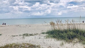 A beach with sand, grass, and the sea under a cloudy sky. - THE BEACH SHACK, a stylish oceanfront townhouse on quiet corner of Indialantic! (Indialantic)