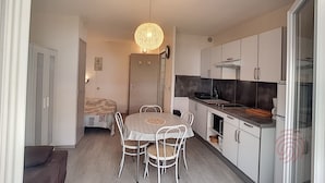 Une cuisine de taille réduite avec des meubles blancs, une table à manger et quatre chaises, ainsi qu’un luminaire suspendu.