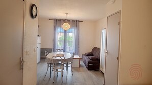 Une pièce comprenant une table à manger, des chaises, un canapé, une petite table et une fenêtre avec des rideaux.