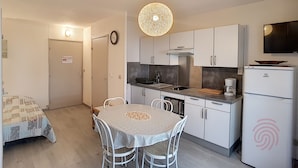 Une cuisine compacte avec des meubles blancs, une table à manger et quatre chaises, un luminaire suspendu et un four encastré.