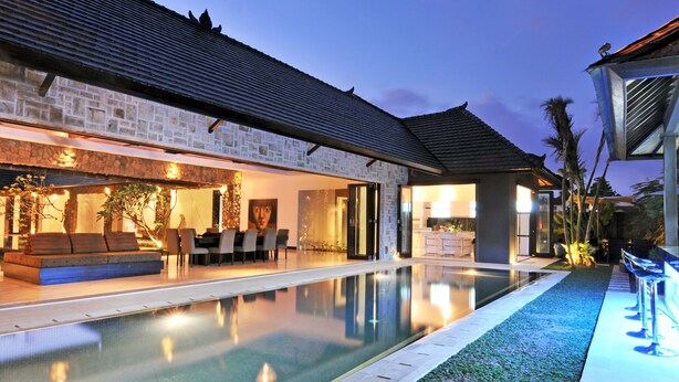 A modern house with a swimming pool, stone exterior, and a well-lit patio area. - Villa Samudra Raya (Seminyak)