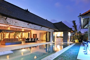 Une maison moderne dotée d’une piscine, d’une façade en pierre et d’un patio bien éclairé.