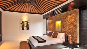 A modern bedroom with a large bed, a stone accent wall, and a ceiling with wooden beams. - Villa Samudra Raya (Seminyak)