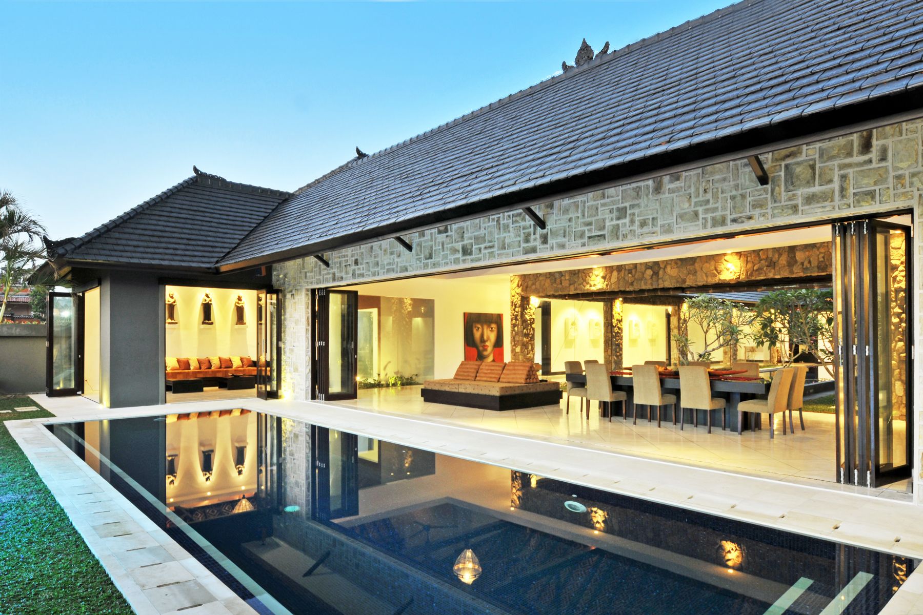A modern house with a swimming pool, stone exterior, and a dining area with outdoor seating.