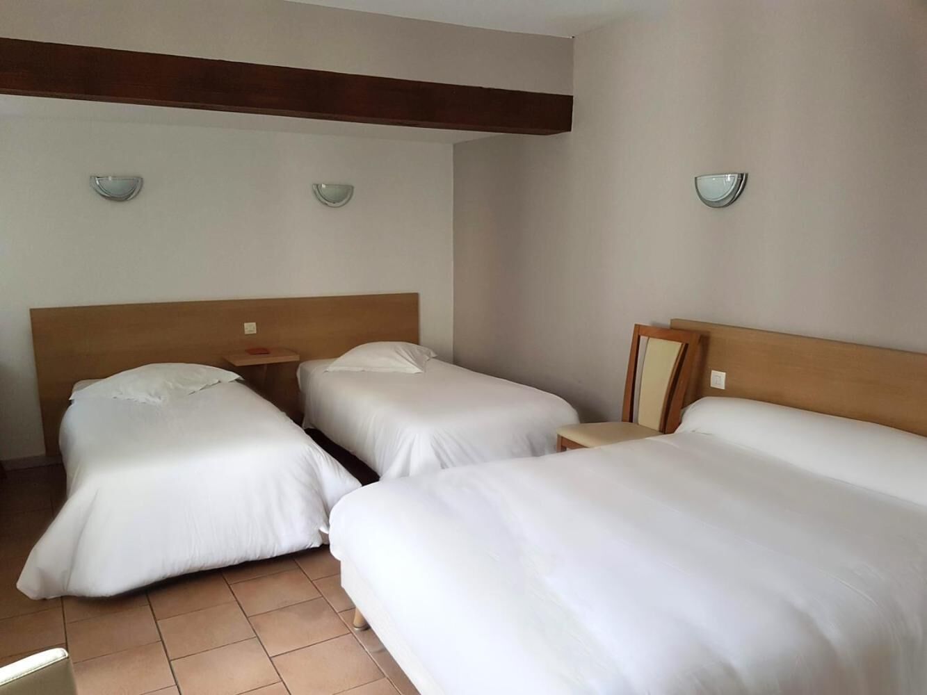 Une chambre d’hôtel avec trois lits simples, une tête de lit en bois et une petite table.