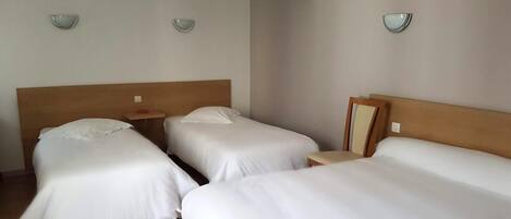 A hotel room with three single beds, a wooden headboard, and a small table.