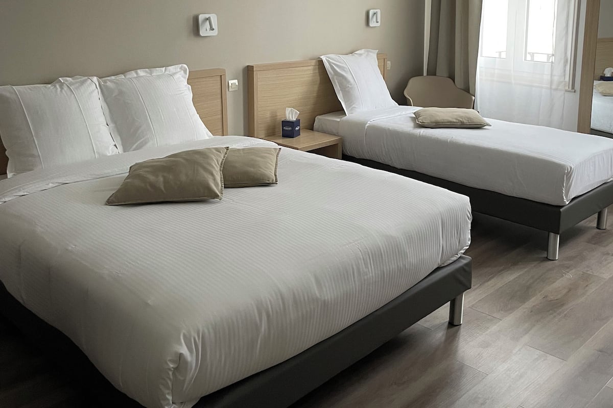 A hotel room with two beds, a wooden headboard, a bedside table with a tissue box, and a window with curtains.