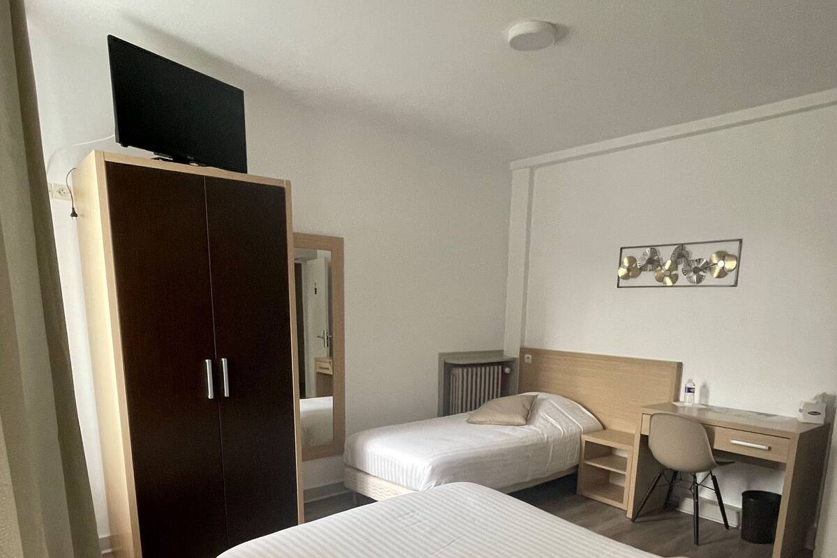 A hotel room with two beds, a wardrobe, a desk, and a chair.