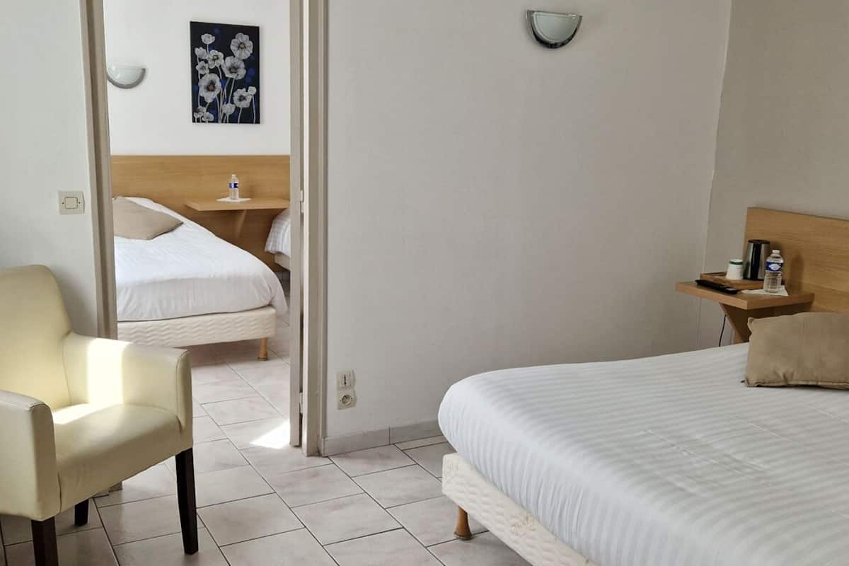 A hotel room with a bed, a chair, a bedside table, and a wall-mounted light fixture.
