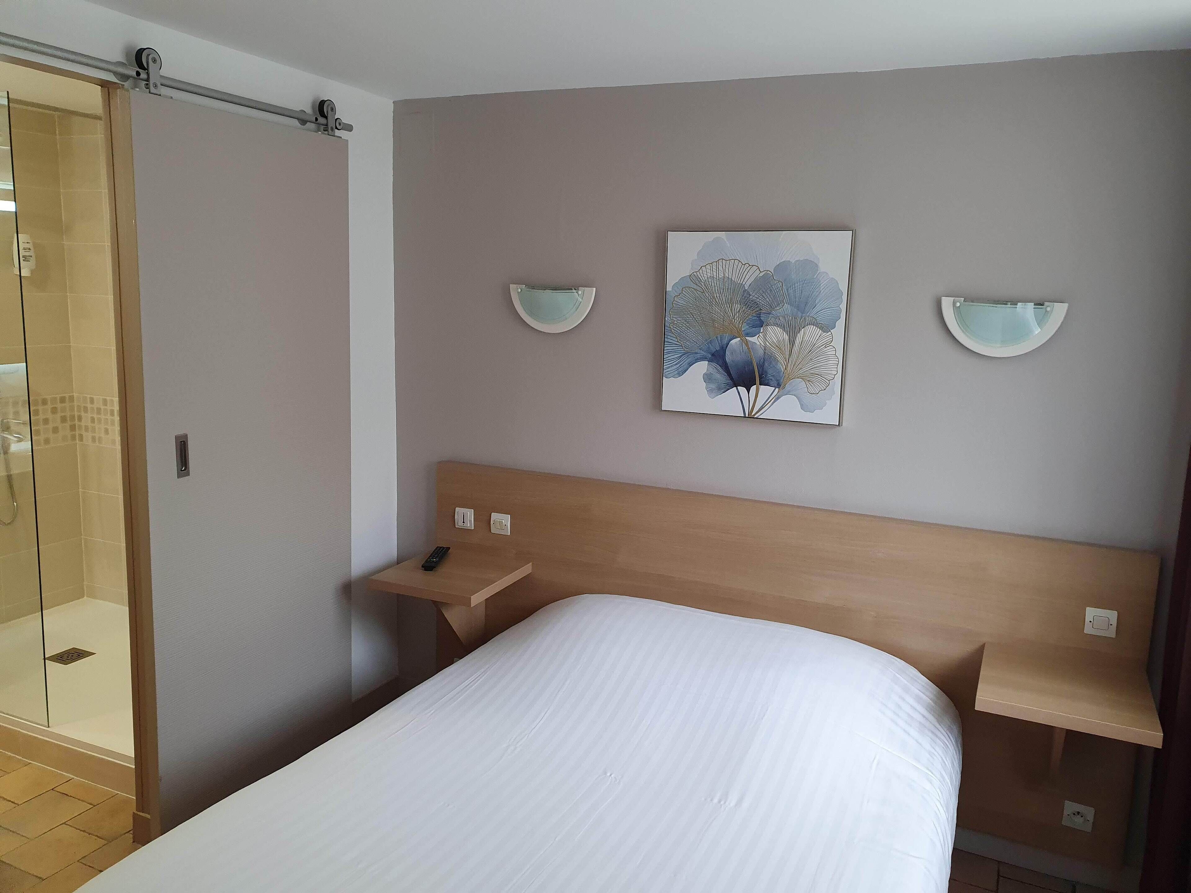 Una habitación de hotel con cama, mesita de noche, obra de arte en la pared y zona de ducha.