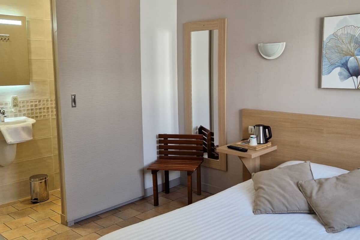 A hotel room with a bed, a wooden nightstand, a wall-mounted sink, and a chair.