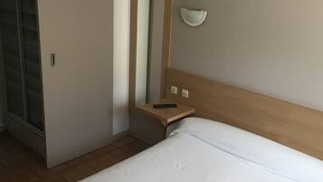 A hotel room with a bed, a bedside table with a remote control, a mirror, and a wall-mounted light fixture.