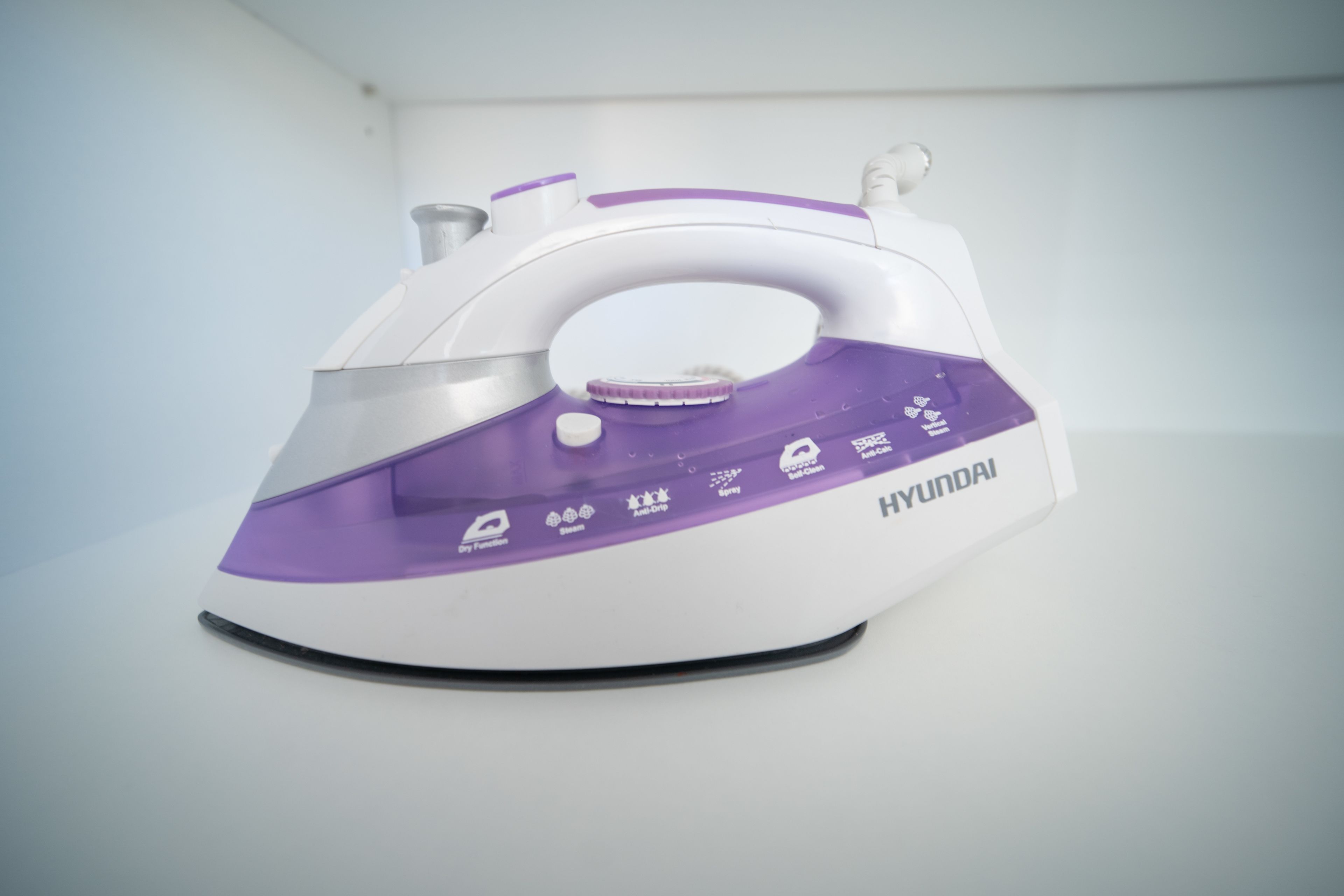 Um ferro elétrico branco e roxo, com a marca "HYUNDAI" visível na lateral.