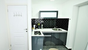 A compact kitchen with a white door, black tiled backsplash, a stainless steel sink, and a gas stove. - YalaRent Designed 1BR Apartments - Families only (Eilat)
