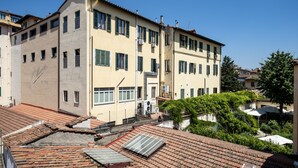 Um edifício com vários andares, telhado plano, diversas janelas e um pátio com vegetação.