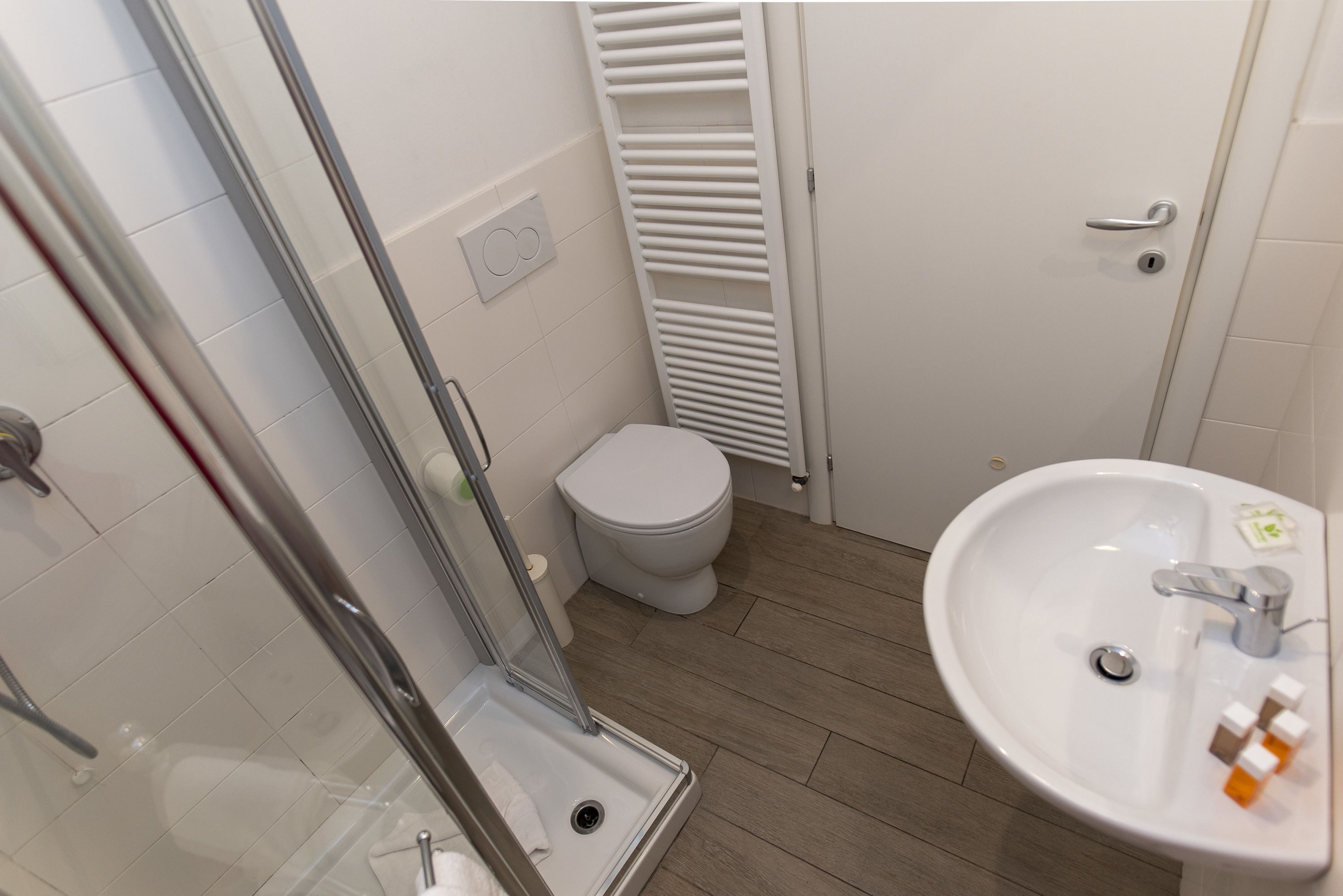 A bathroom with a glass shower enclosure, a toilet, and a sink with toiletries.