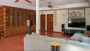 A spacious living room with a large sofa, a television, and a ceiling fan. - Xanadu Pool Villa at Phala (Ban Chang)