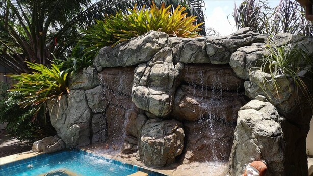 A swimming pool with a rock waterfall feature and a decorative statue. - Xanadu Pool Villa at Phala (Ban Chang)