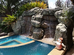 A swimming pool with a rock waterfall feature and a decorative statue. - Xanadu Pool Villa at Phala (Ban Chang)