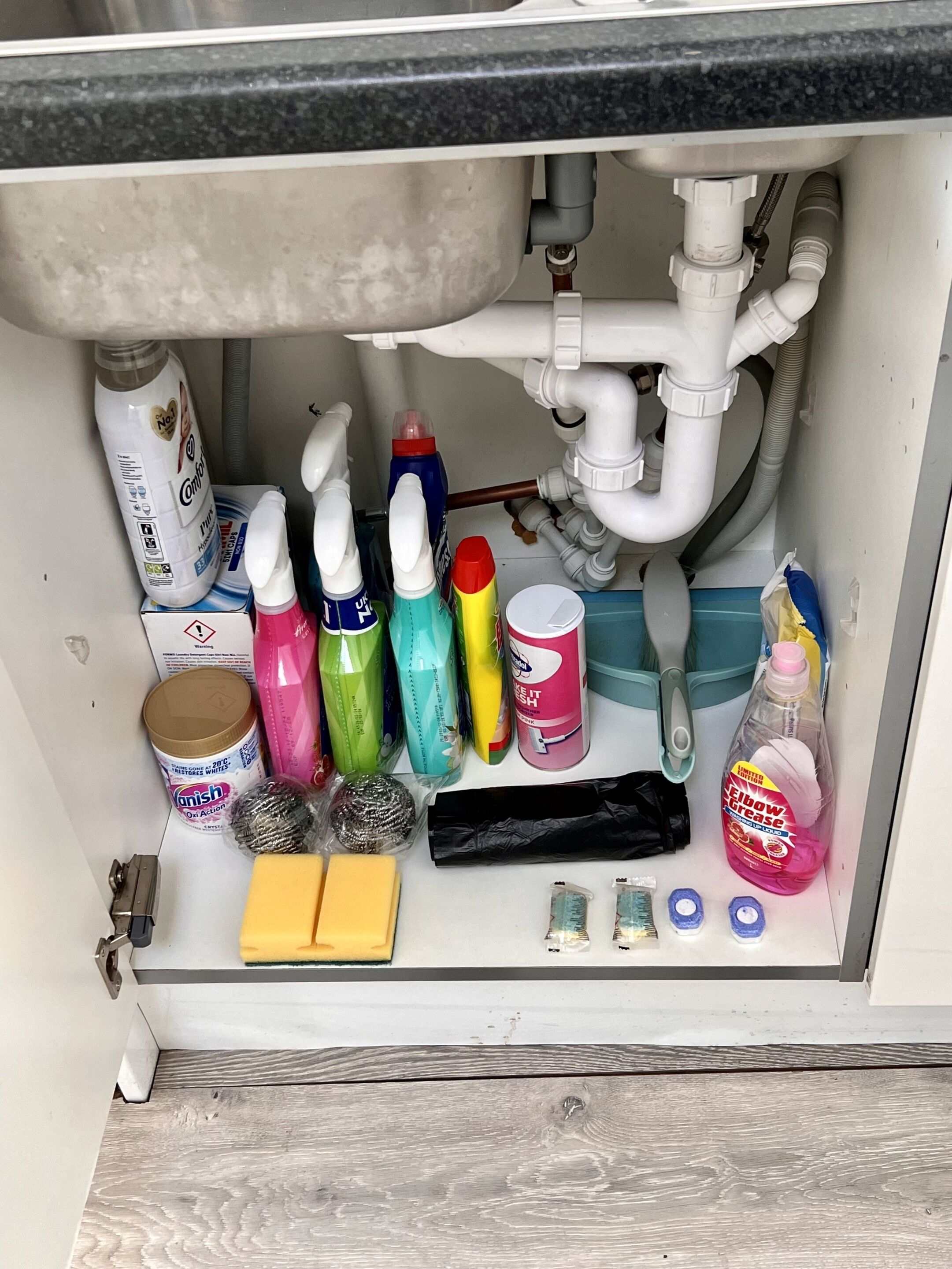 Una zona de pila con varios productos de limpieza, incluyendo botellas de detergente, un bote de lavavajillas y una botella de limpiador multiusos.