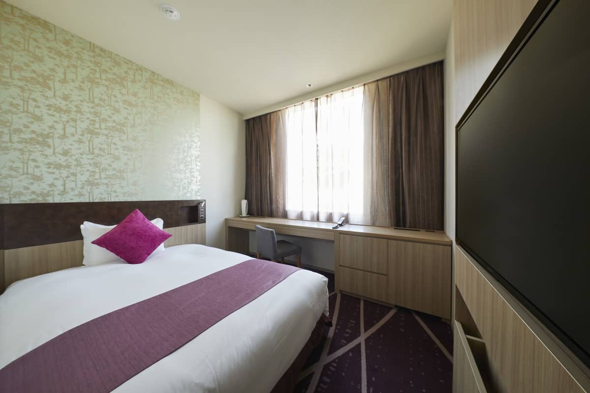 Une chambre d’hôtel avec un grand lit, un bureau, une chaise, une télévision et une fenêtre avec des rideaux.