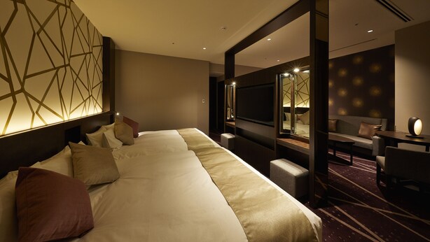 Hotelkamer met een groot bed, een bureau, een stoel, een televisie en een decoratieve wand.