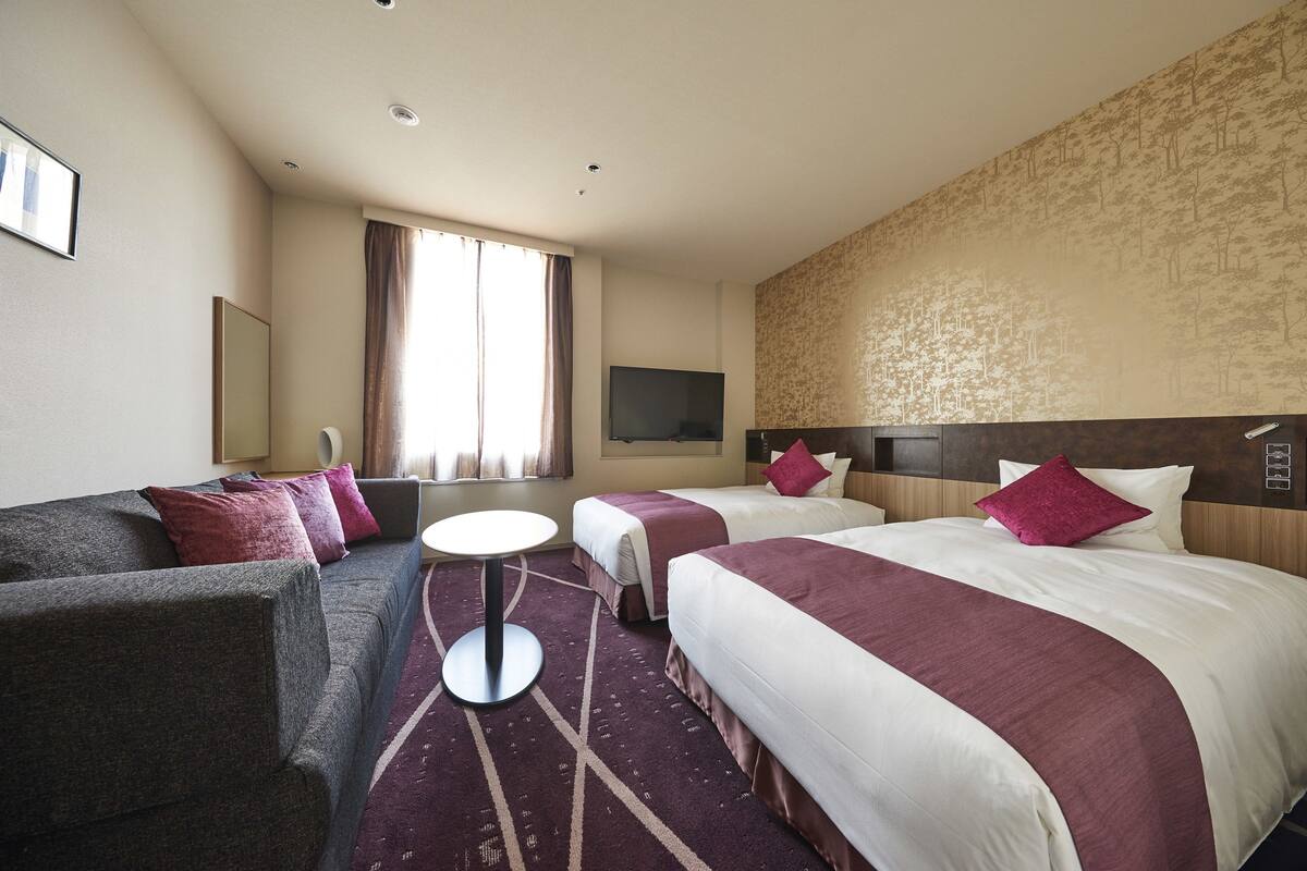 Une chambre d’hôtel avec deux lits, un canapé, une télévision et une fenêtre avec des rideaux.