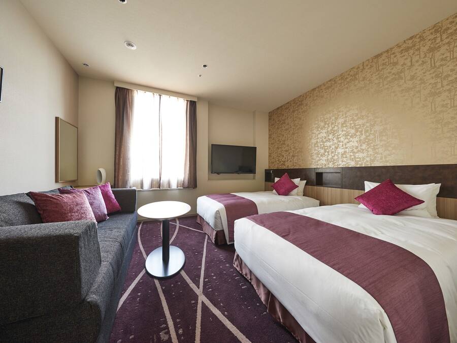 Een hotelkamer met twee bedden, een bank, een televisie en een raam met gordijnen.
