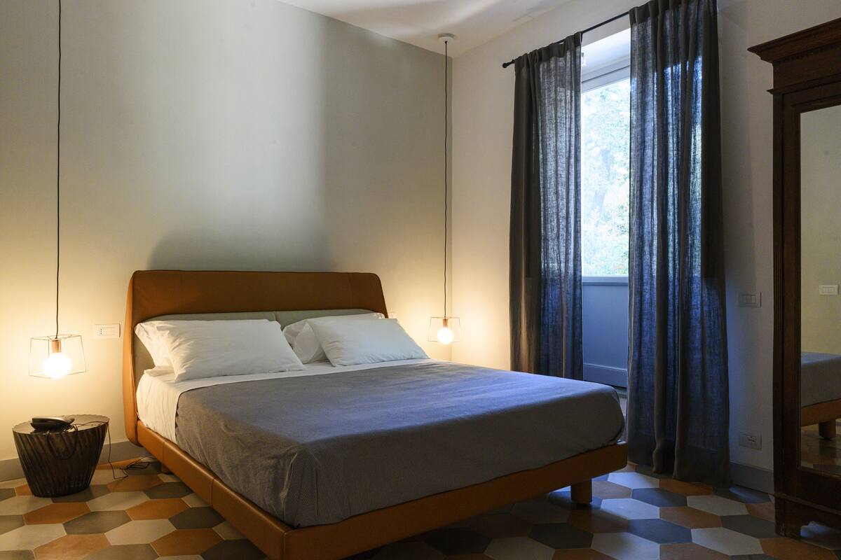 A neatly made bed with a wooden headboard, two bedside lamps, and a window with curtains.