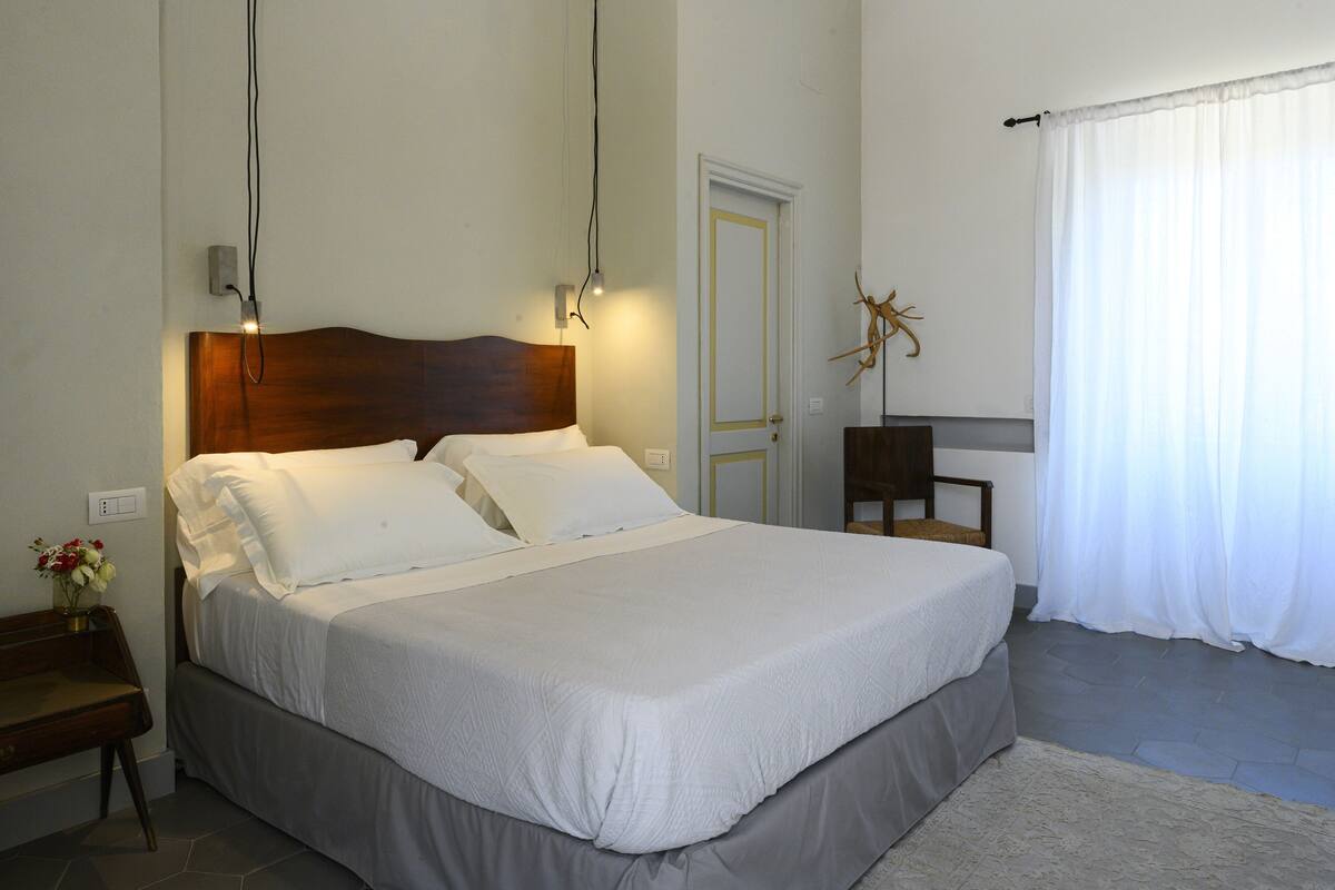 A neatly made bed in a room with a wooden headboard, a bedside table with a lamp, and a door with a decorative key on the wall.