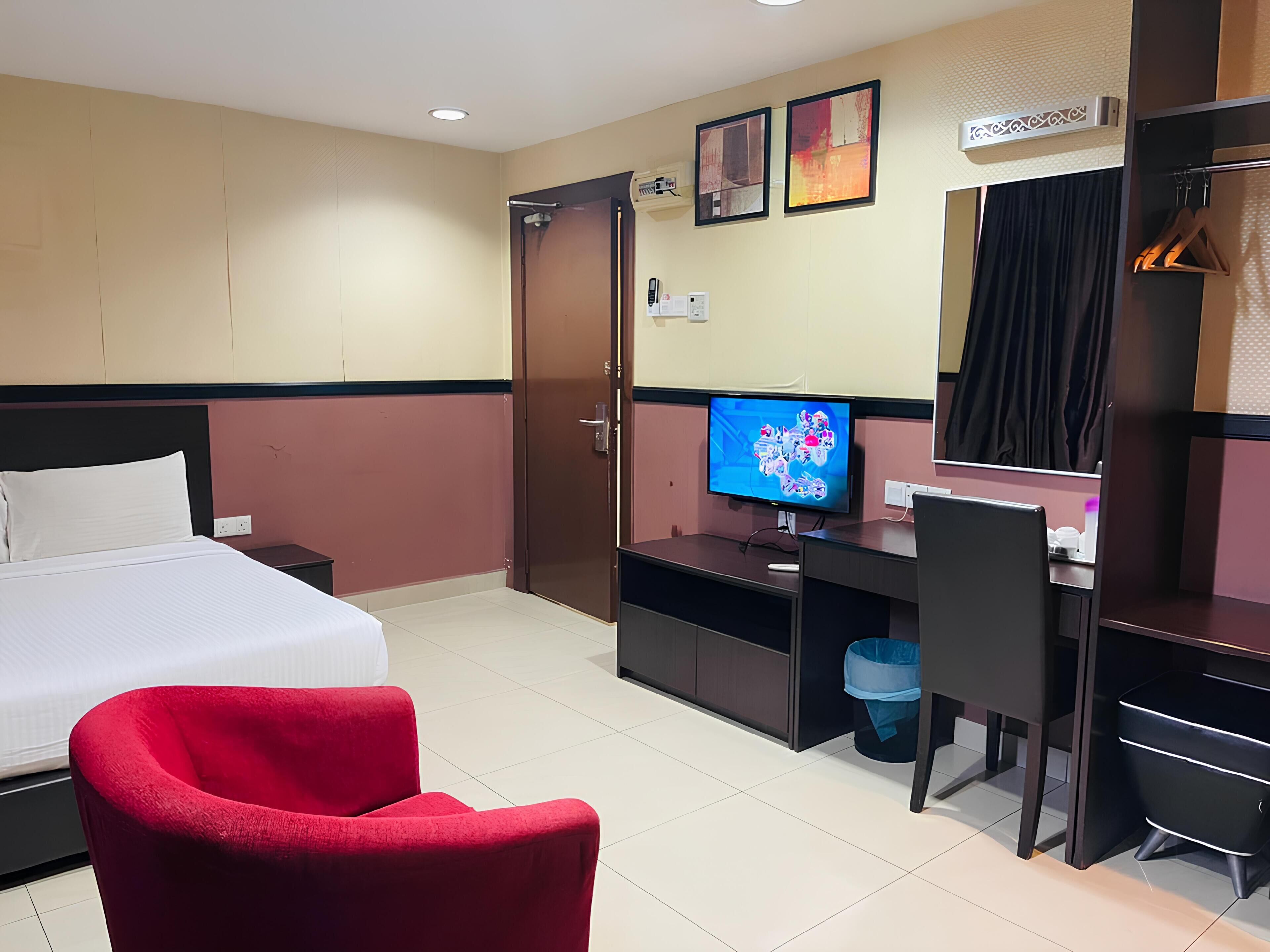 A hotel room with a bed, a desk with a computer, a TV, and a red chair.