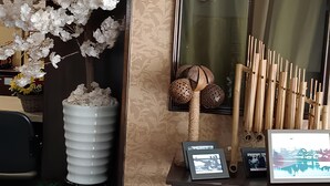 A reception area with a decorative white artificial tree, a wooden cabinet with framed photos, and a display of wooden chopsticks. - Hotel Sayang (Kulai)