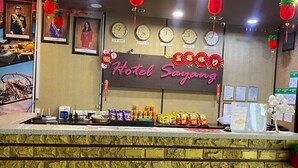 A hotel reception desk with clocks, a neon sign, and various snacks. - Hotel Sayang (Kulai)