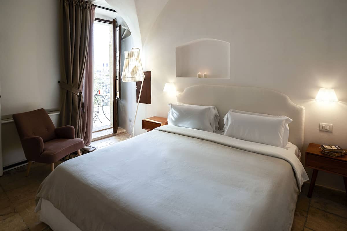 Una habitación de hotel con una cama grande, una silla, una mesita de noche y una lámpara.