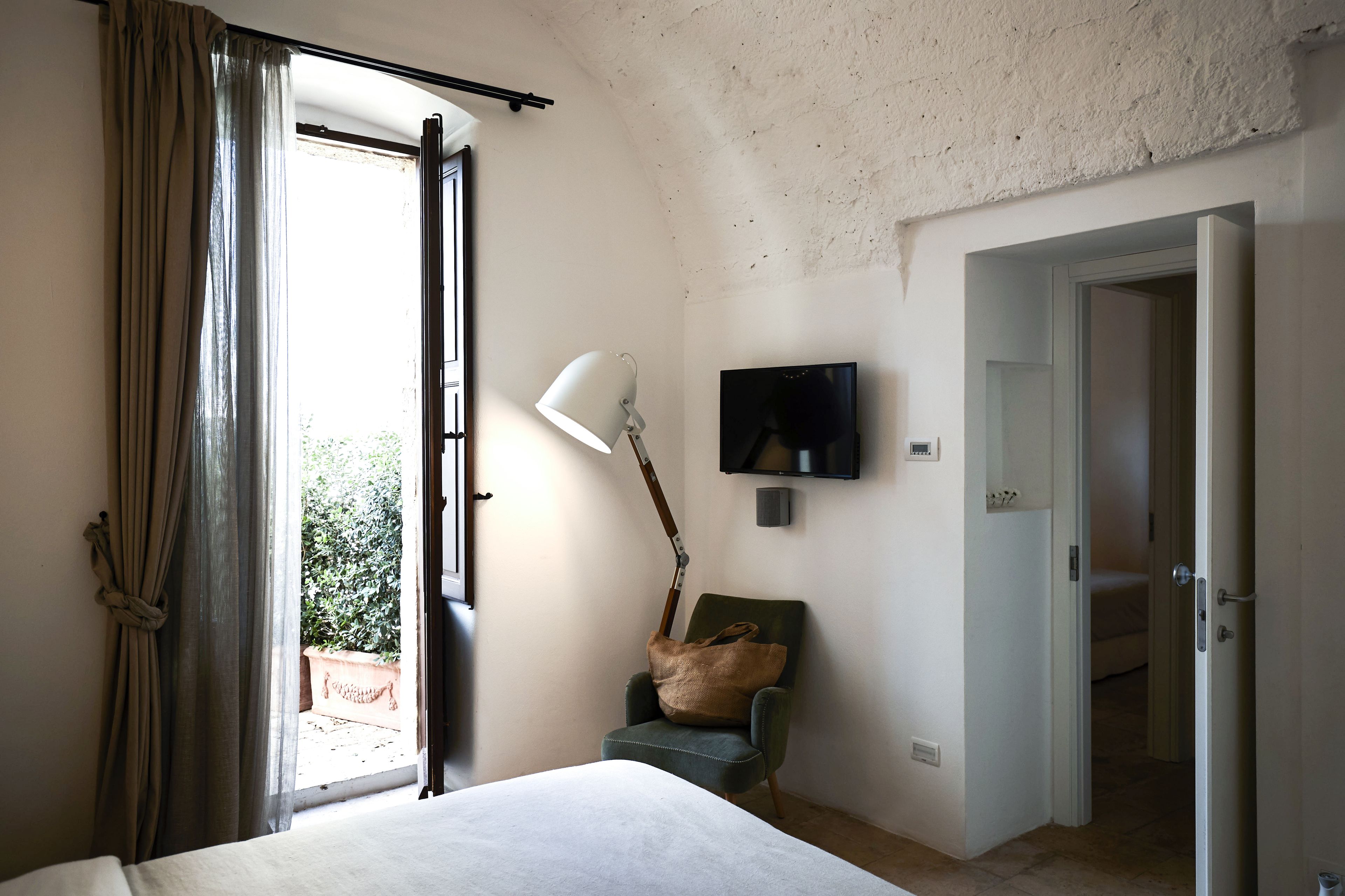 Un dormitorio con cama, una silla, un televisor y una puerta que da a otra habitación.