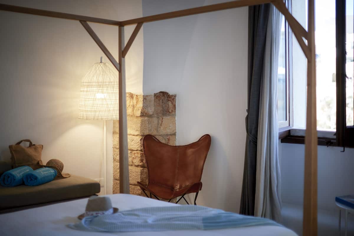 Un dormitorio con una cama, un sillón de cuero marrón, una lámpara y una pared de piedra.