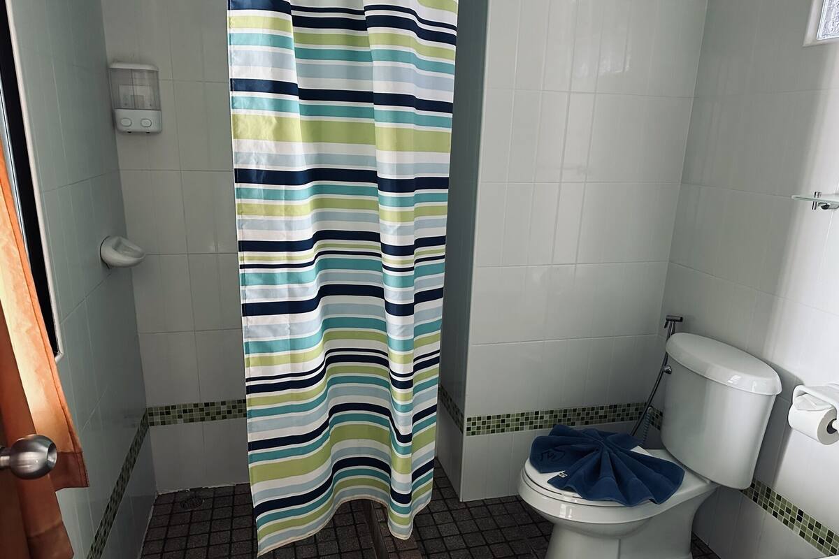 A bathroom with a striped shower curtain, a toilet, and a tiled floor.