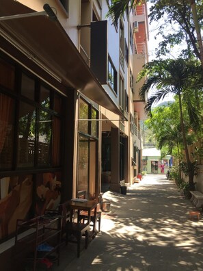 A narrow alleyway with a building on one side and a tree-lined street on the other. - Smile Home (Patong)