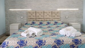 A hotel room with a bed, headboard, nightstands, and a painting of a beach scene. - B&B Catania Mare (Catania)