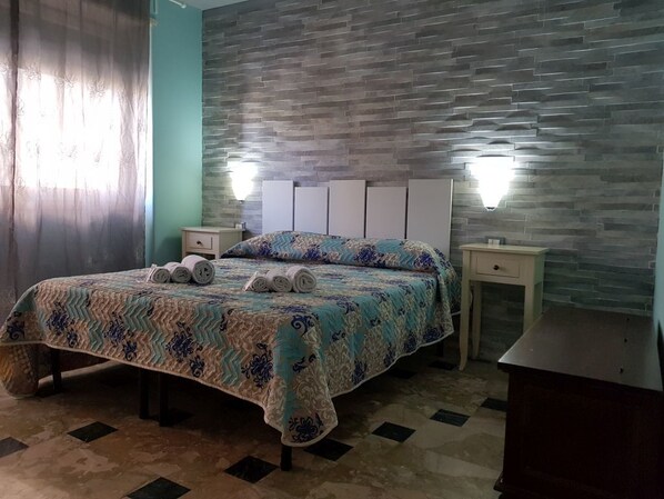 A bedroom with a bed, two nightstands, a dresser, and a stone-patterned wall. - B&B Catania Mare (Catania)
