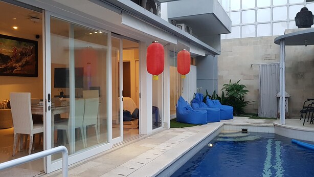 A modern indoor pool area with a glass wall, blue bean bag chairs, and a dining area with a table and chairs. - Villa Fei (Jimbaran)