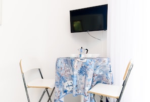 A room with a table covered by a nautical-themed tablecloth, a flat-screen TV mounted on the wall, and two chairs with wooden frames. - Casa Laura Blu (Sant'Agnello)