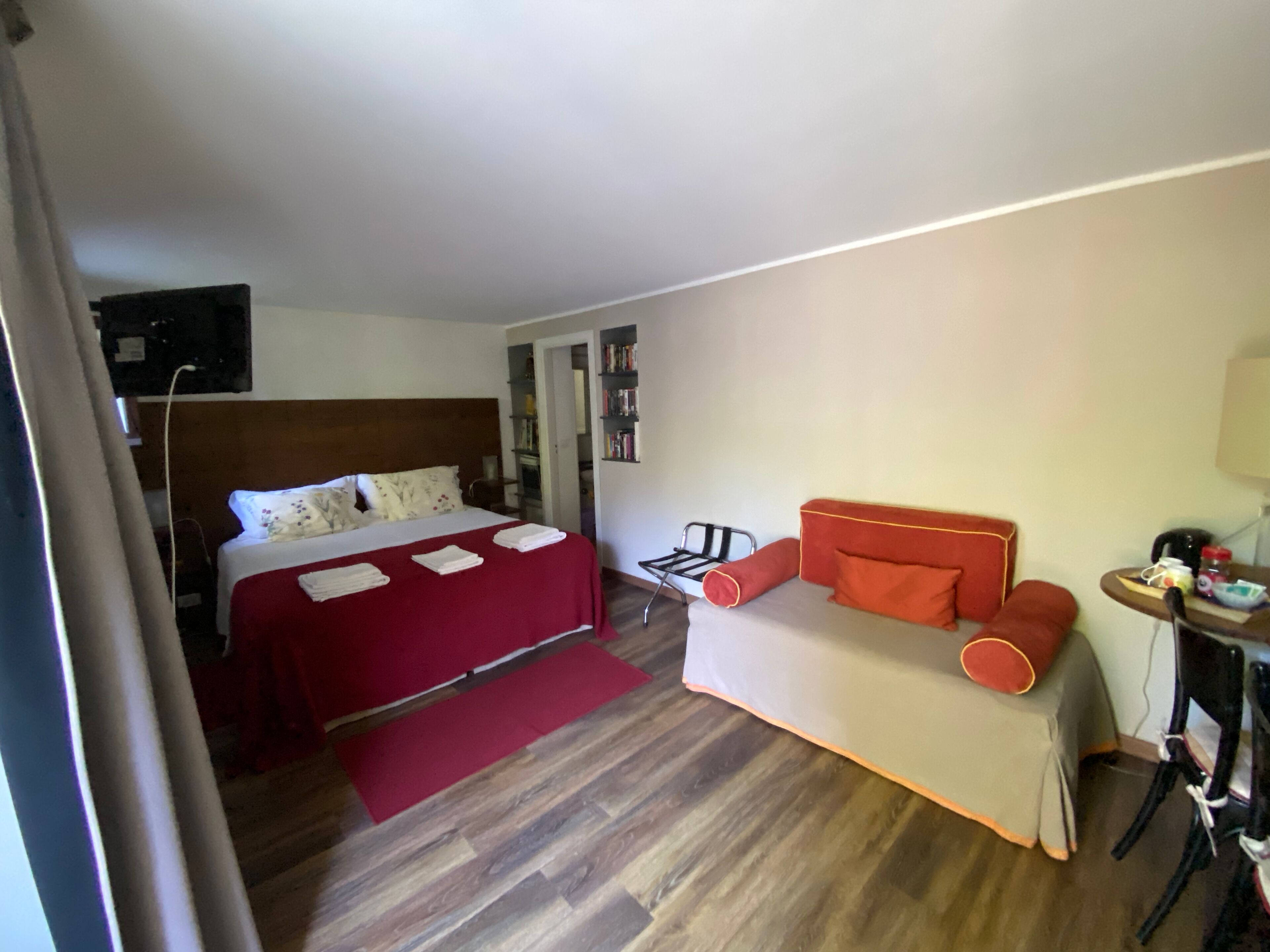 A hotel room with a bed, a sofa, a small table, and a bookshelf.