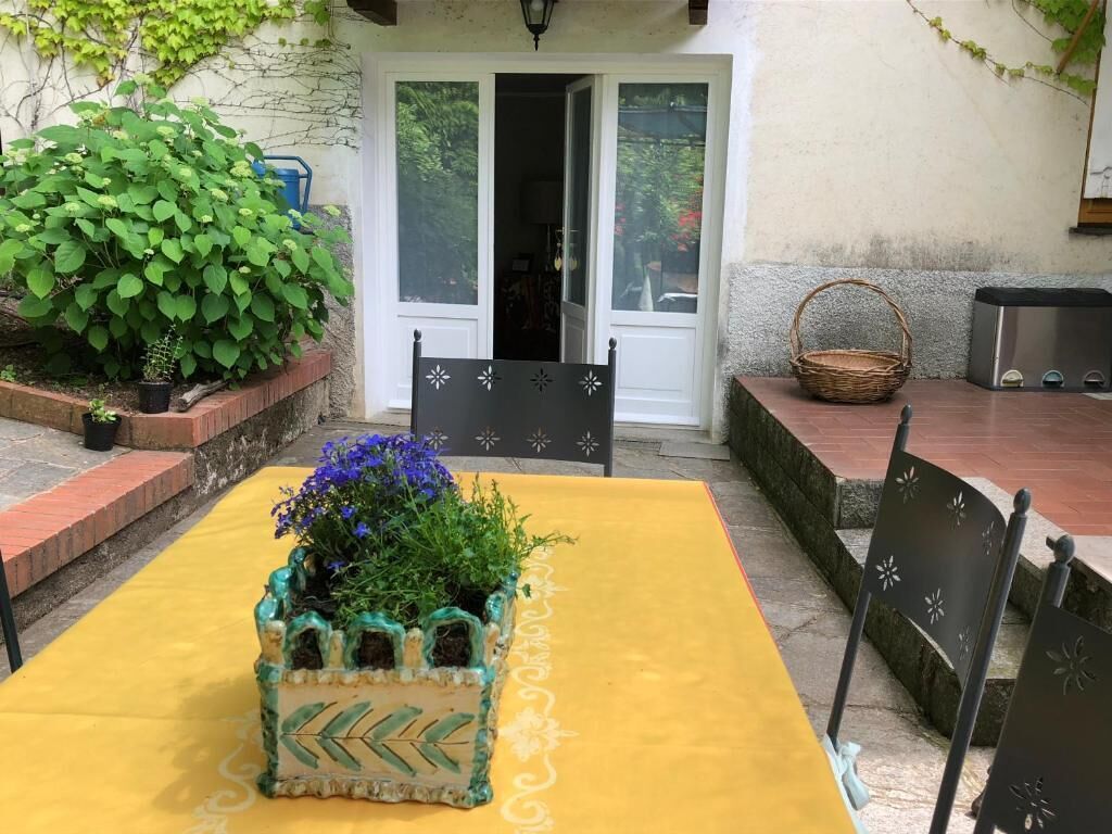 An outdoor patio with a yellow table, chairs, a decorative planter with flowers, and a basket.