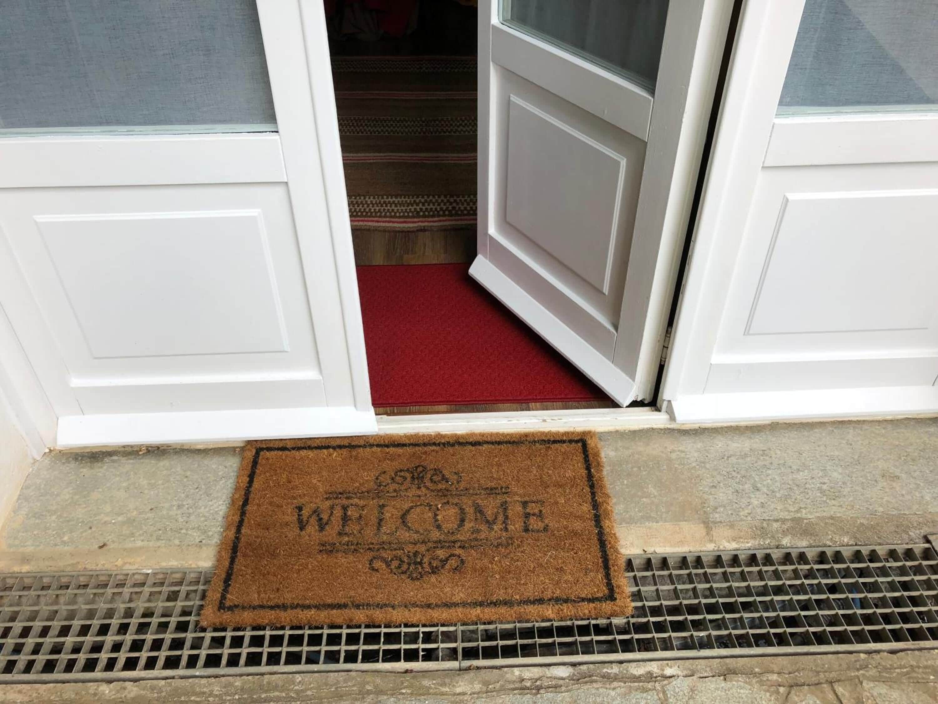 A white door with a red carpet leading to a room. A brown doormat with "WELCOME" is placed at the entrance.