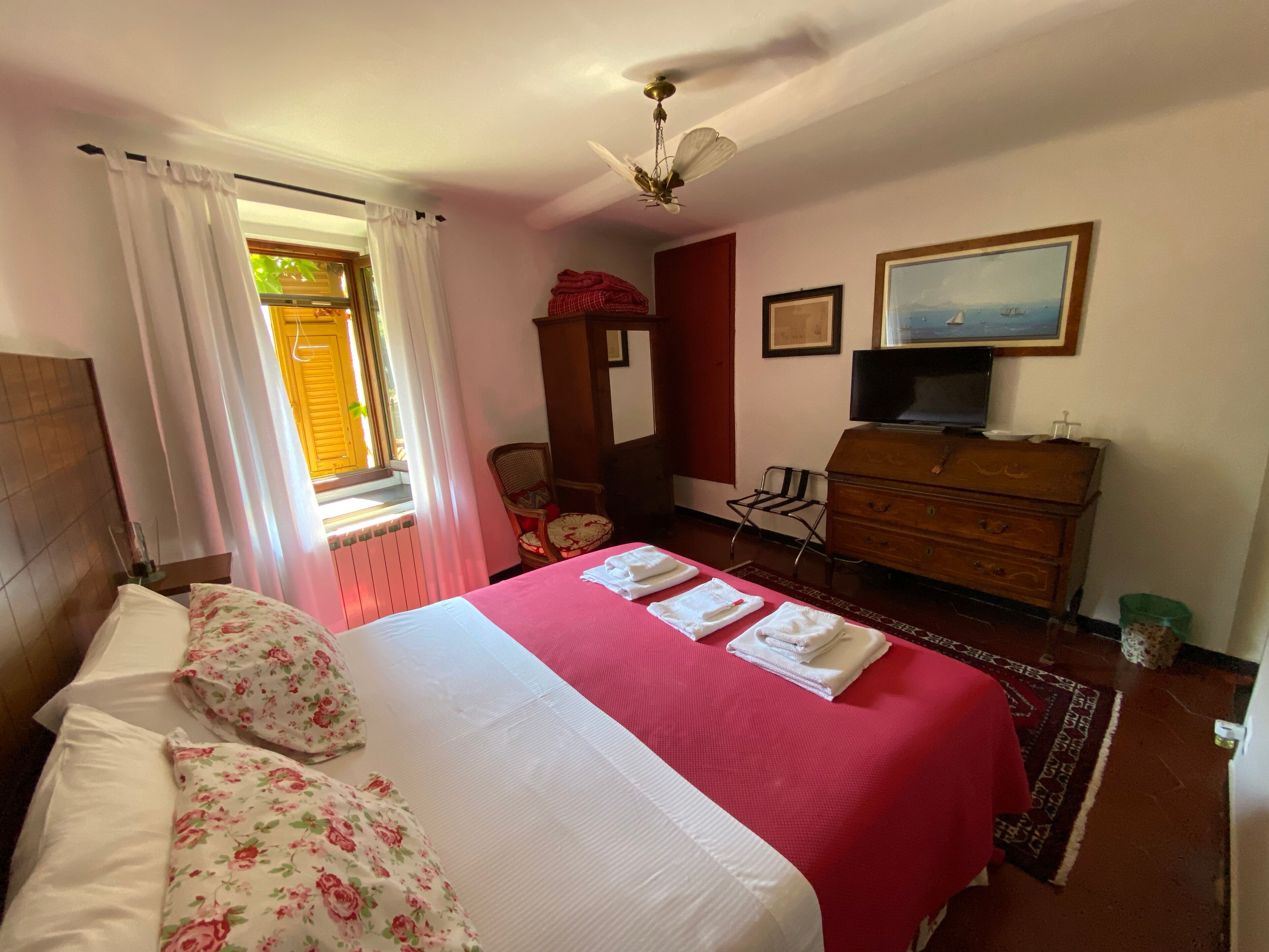 A bedroom with a bed, a dresser, a chair, a television, and a window with curtains.