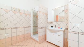 Un baño con ducha, lavamanos y espejo.