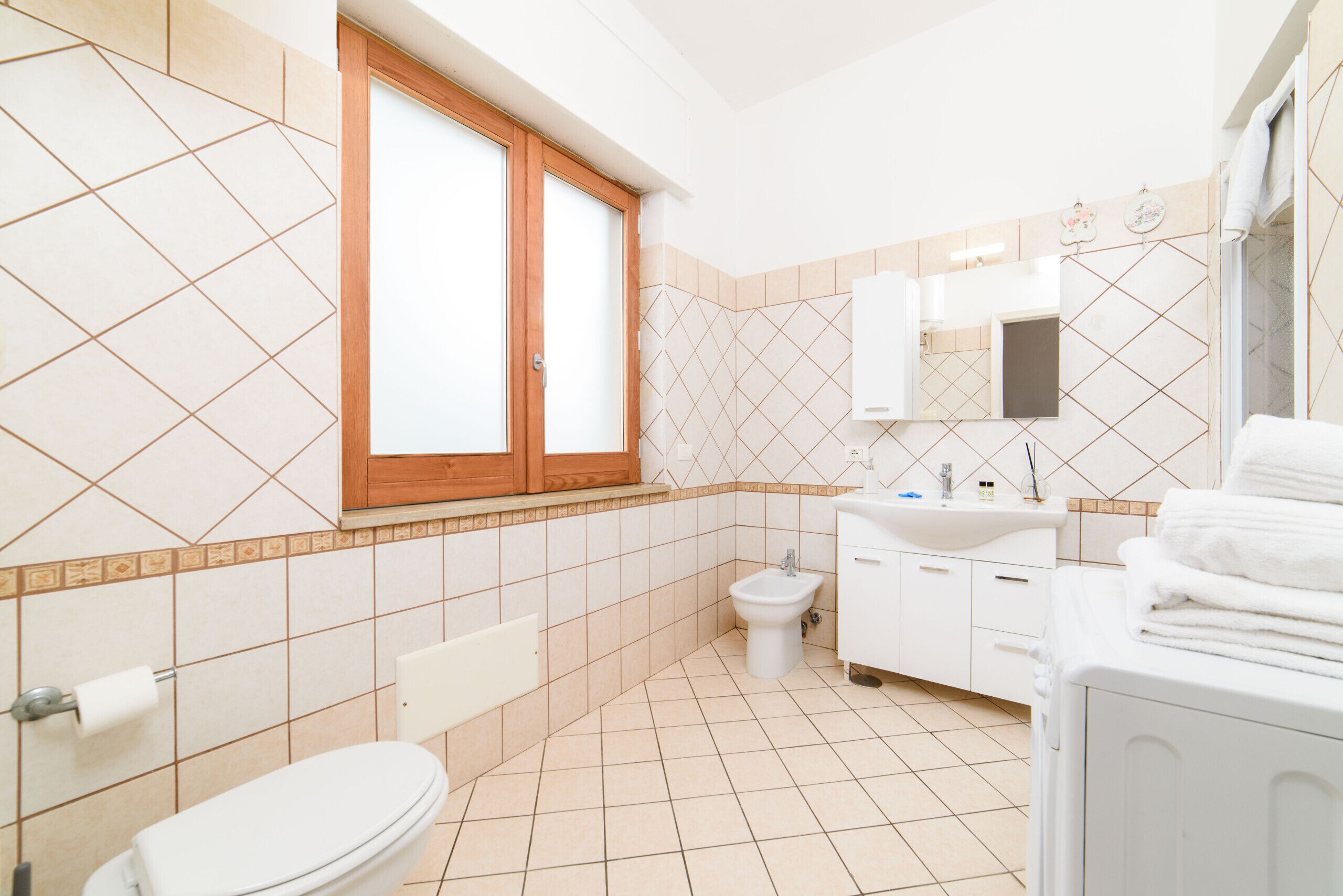 A modern bathroom with a toilet, bidet, sink, and stacked towels.