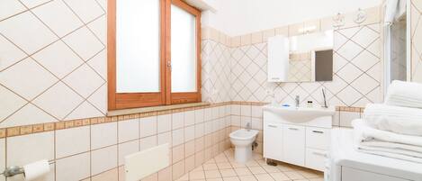 A modern bathroom with a toilet, bidet, sink, and stacked towels.
