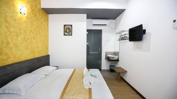Una habitación de hotel con una cama, un televisor montado en la pared, un lavamanos y una puerta que da a otra habitación.
